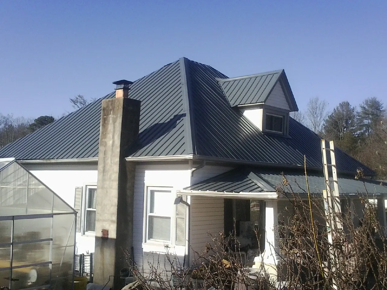 Dark blue standing seam metal roof on a white farmhouse with dormer — Slate & Tile Roof Repair by Roofing Brothers in Toone