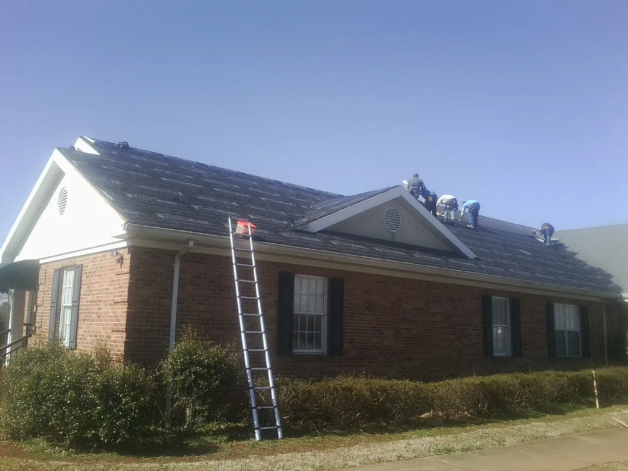 Crew tearing shingles off a brick ranch roof with a ladder set — Emergency Roof Repair work by our crew in Toone