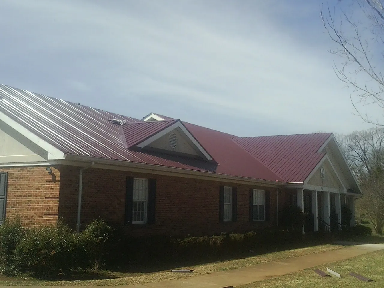 Red metal roof with gabled entries on a long brick building, from a Hail Damage Roof Repair job in Toone