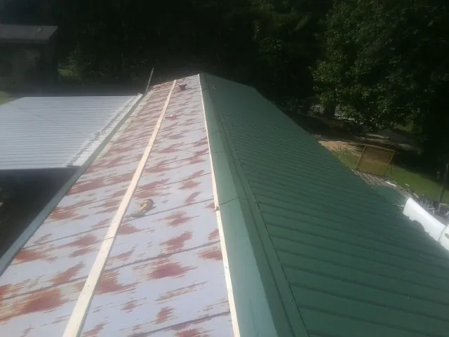 Old rusted panels beside newly installed green metal roofing — Wind Damage Roof Repair by Roofing Brothers in Toone