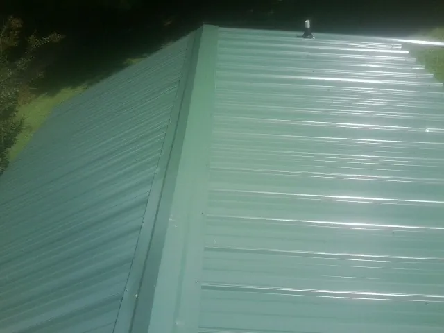 New green metal panels meeting at the ridge of a roof — Flat Roof Repair work by our crew in Toone