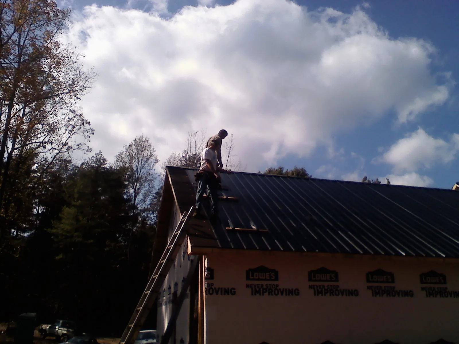 Roofer fastening dark metal panels high against a cloudy sky, from a Roof Inspection job in Toone