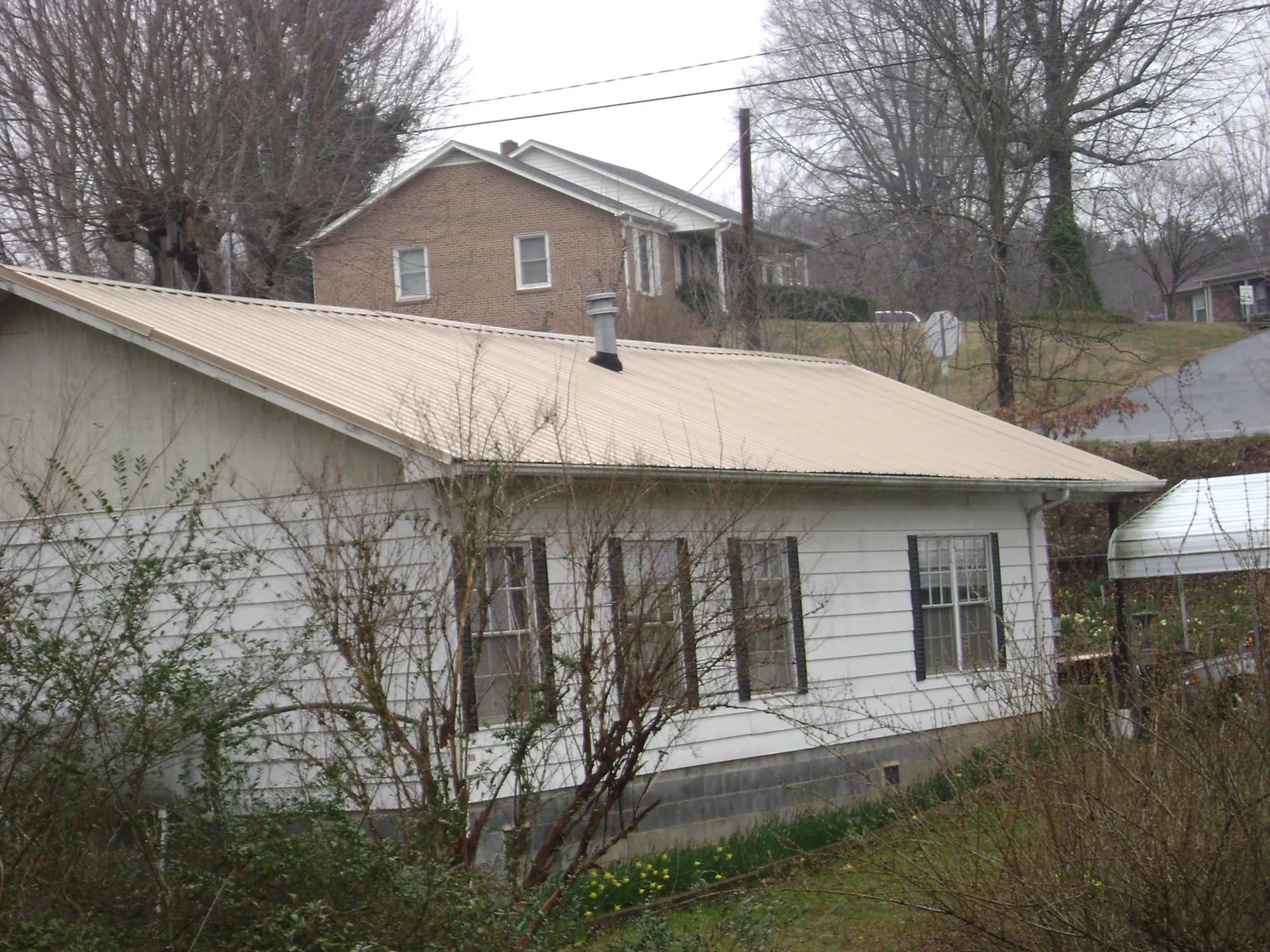 Tan metal roof on a white sided house set into a hillside — Commercial Roofing by Roofing Brothers in Toone