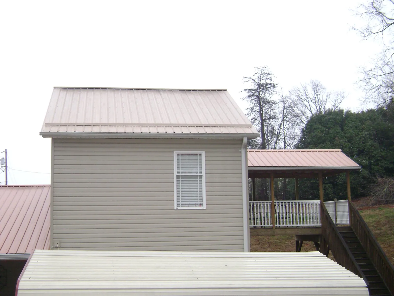 Tan metal roofs on a two story addition and attached porch, from a Roof Replacement job in Toone